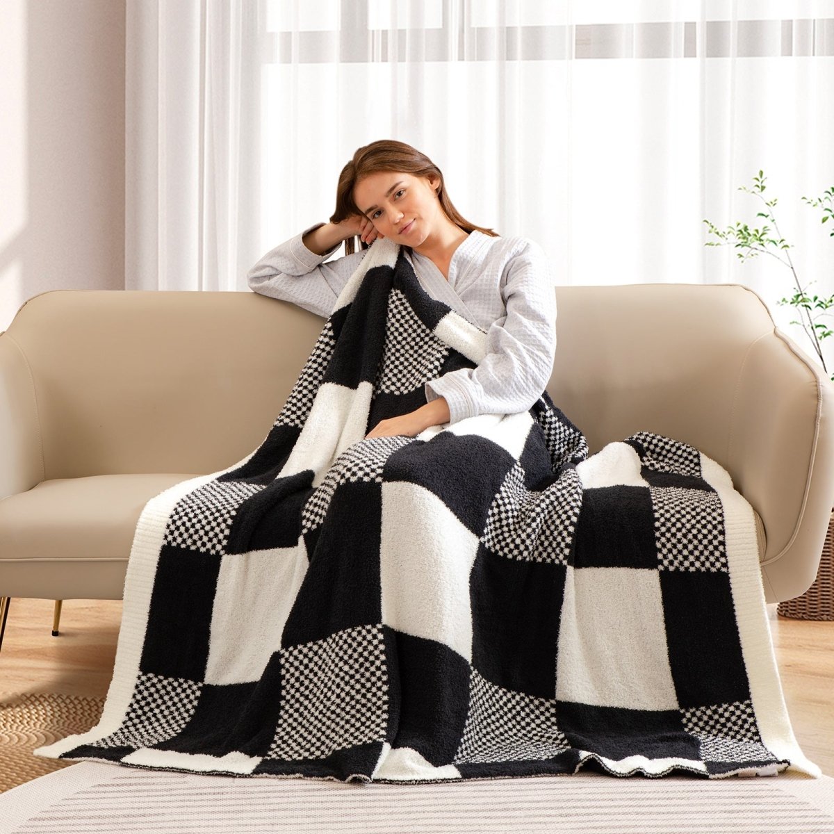 Woman relaxing on a sofa while holding a Checkered Feather Yarn Throw Blanket in Black & White in her hand. #color_Black & White