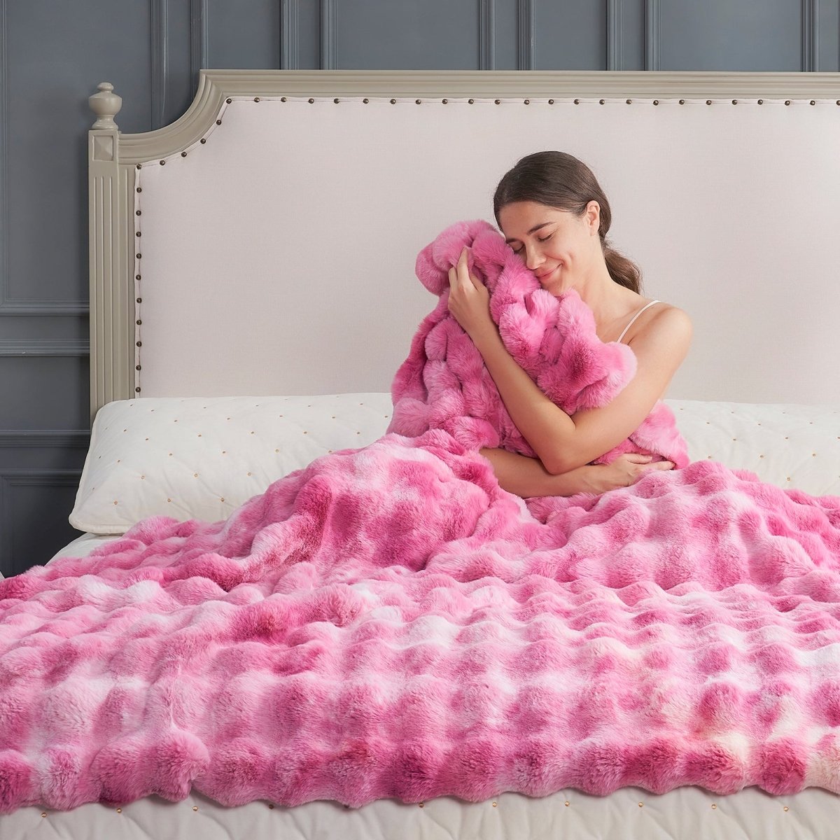 Woman wrapped in a fluffy tie-dye pink faux fur blanket on a bed. #color_Tie-dye Pink