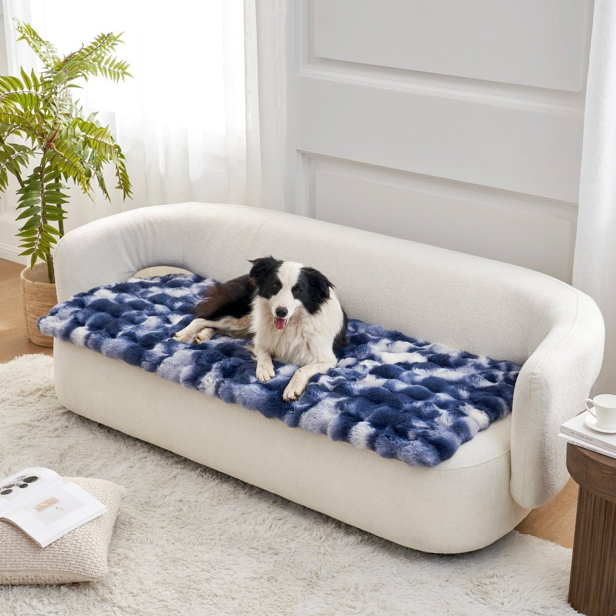 Dog lying on a tie-dye blue couch cover on a white couch in a bright room.#color_Tie-dye Blue