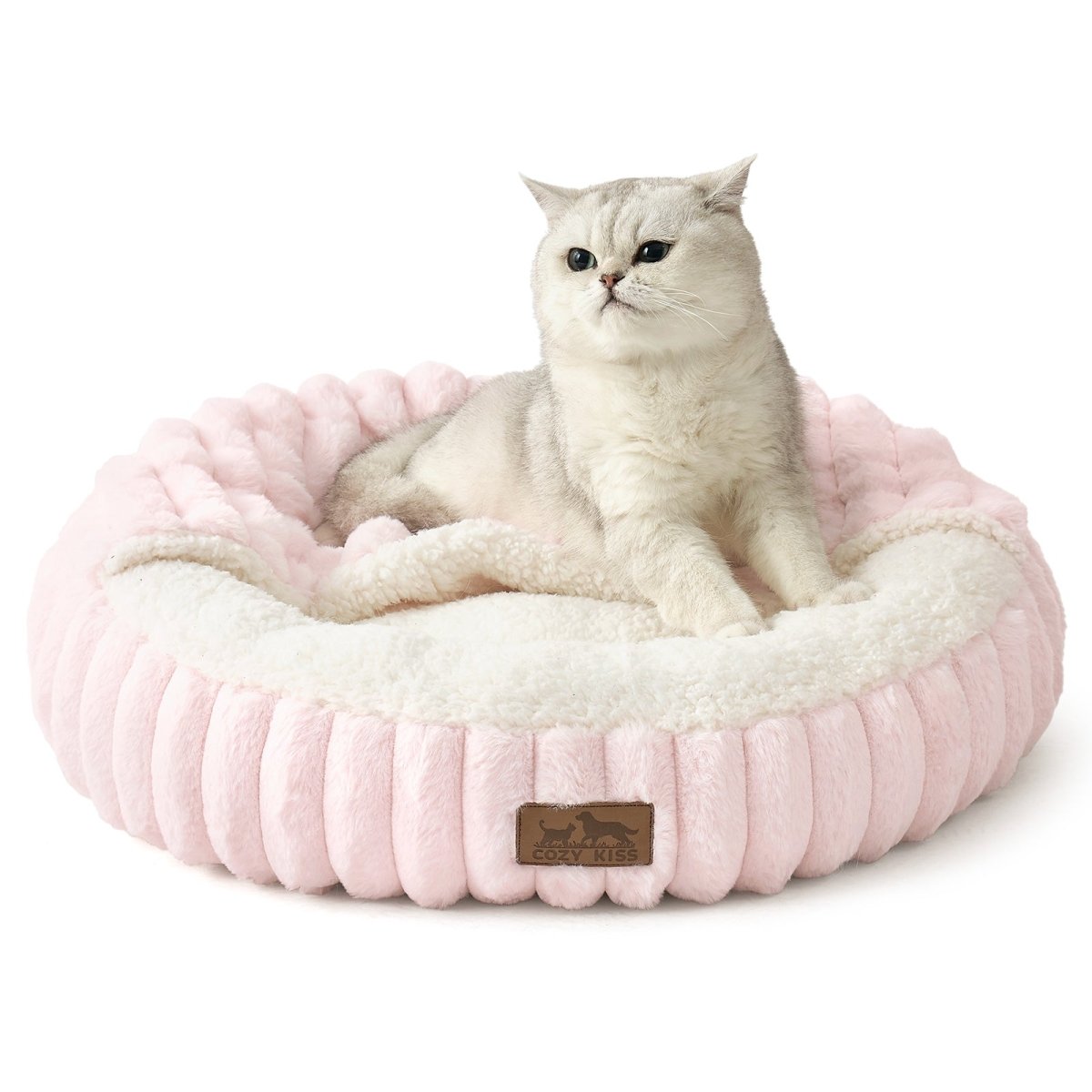 Cat lying on a fluffy pink faux fur pet bed with hooded blanket in a cozy room with wooden furniture and a rug.#color_Pink