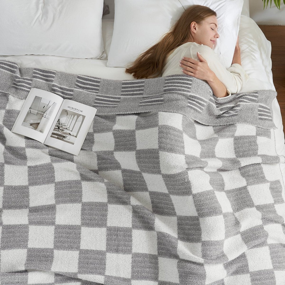 Woman relaxing in bed under a Reversible Heather Checkered Feather Yarn Throw Blanket in Grey, offering warmth and comfort. #color_Grey