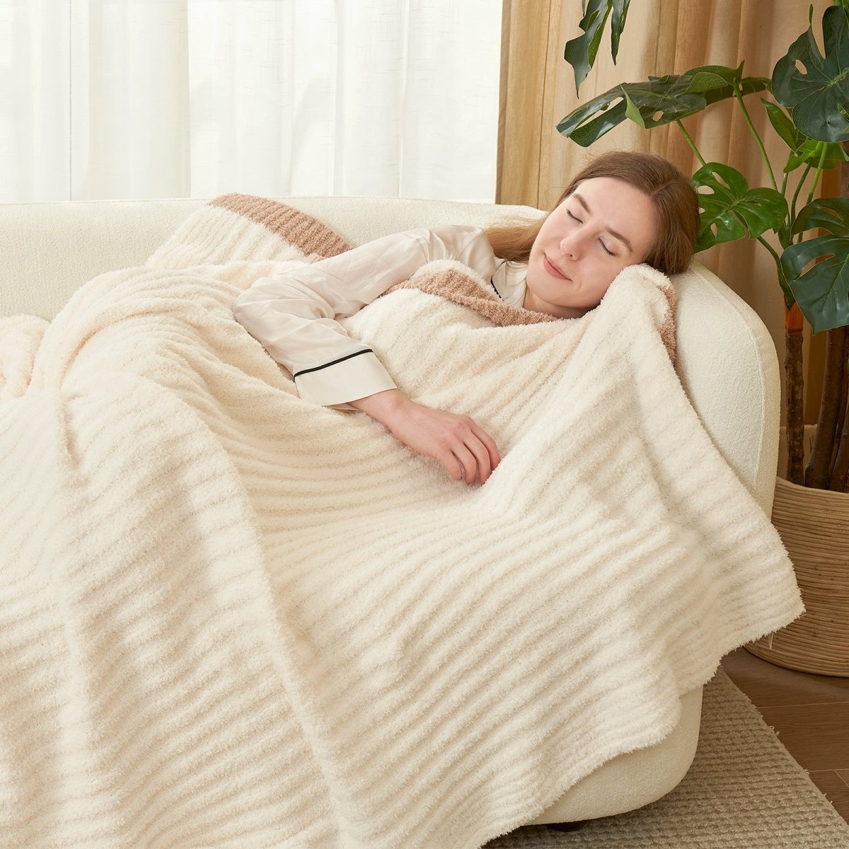 Woman sleeping under Soft Ribbed Feather Yarn Throw Blanket in Cream White on a sofa, enjoying warm and cozy comfort in a bright living room setting. #color_Cream White