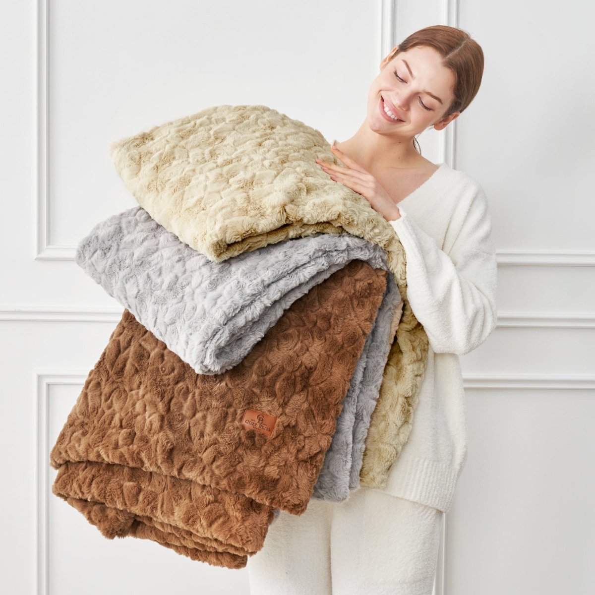 Woman holding a stack of folded blankets against a white wall