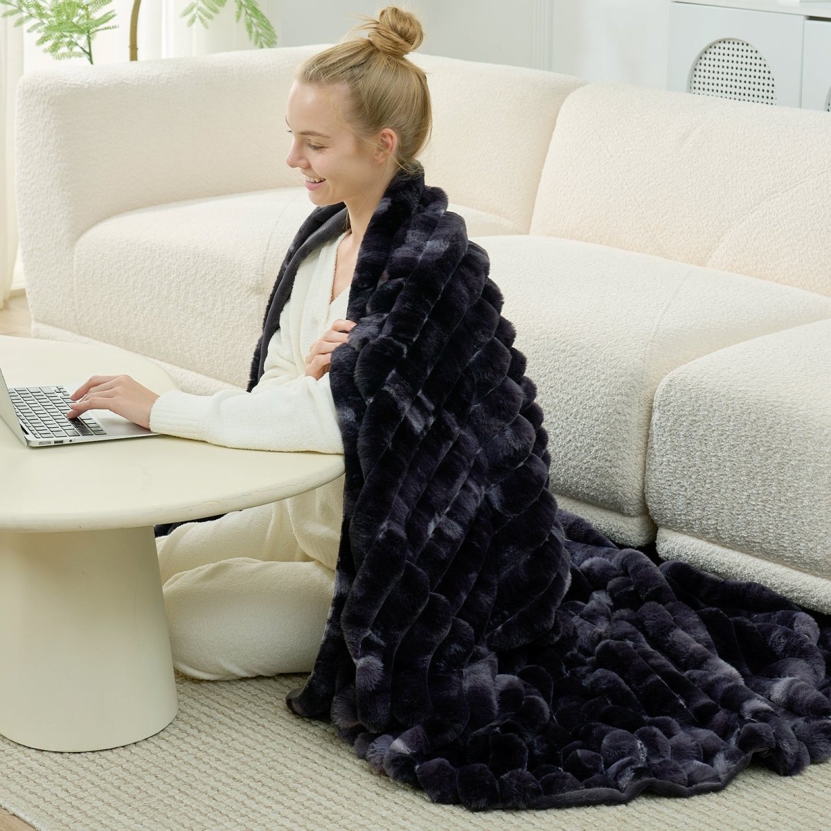 Woman using a laptop on a couch with a dark black faux fur throw blanket draped over her lap. #color_Tie-dye Black