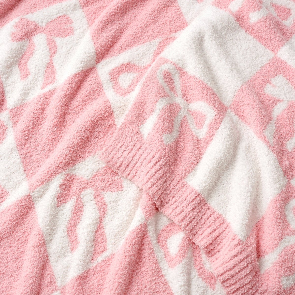 Close-up of Reversible Checkered Bow Feather Yarn Throw Blanket in Pink showcasing plush feather yarn texture, bow pattern and knit edging detail. #color_Pink