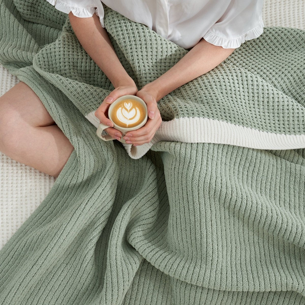 Woman wrapped in a Chenille Waffle Knit Throw Blanket in Sage Green, enjoying a cup of coffee. #color_Sage Green