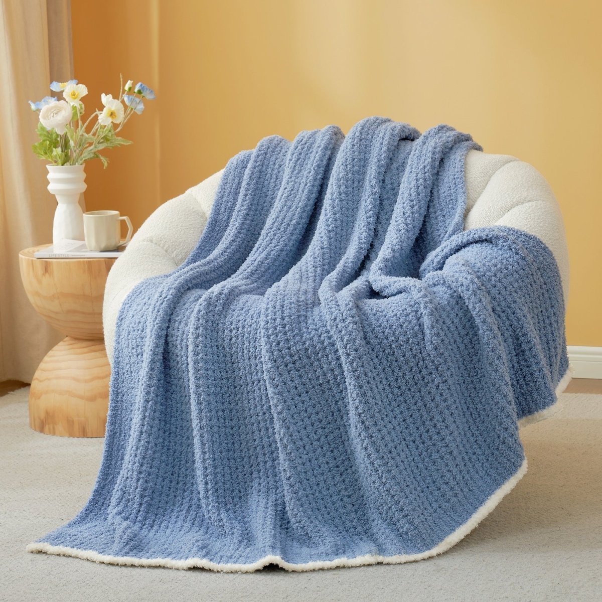 Dark Blue textured blanket draped over a chair with a side table and flowers in the background. #color_Dark Blue