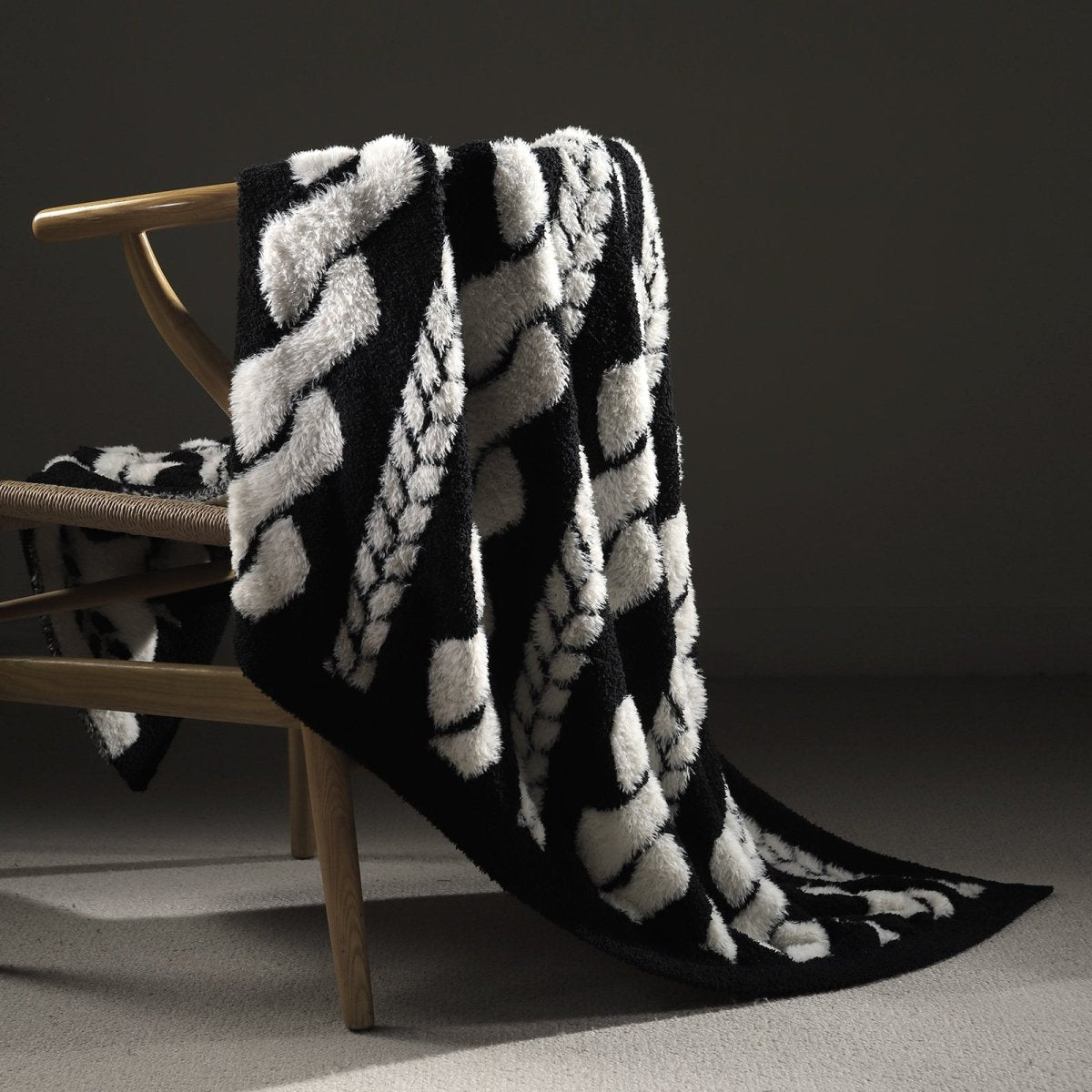 Faux Mink Cable Knit Throw Blanket in Black draped over a chair, showcasing plush texture and elegant cable knit design. #color_Black
