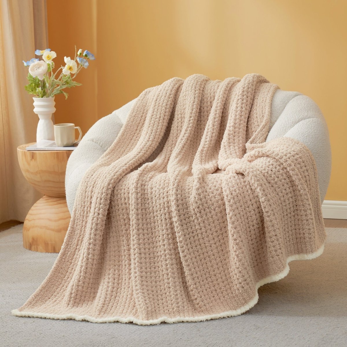 Light Brown textured blanket draped over a chair with a side table and flowers in the background. #color_Light Brown