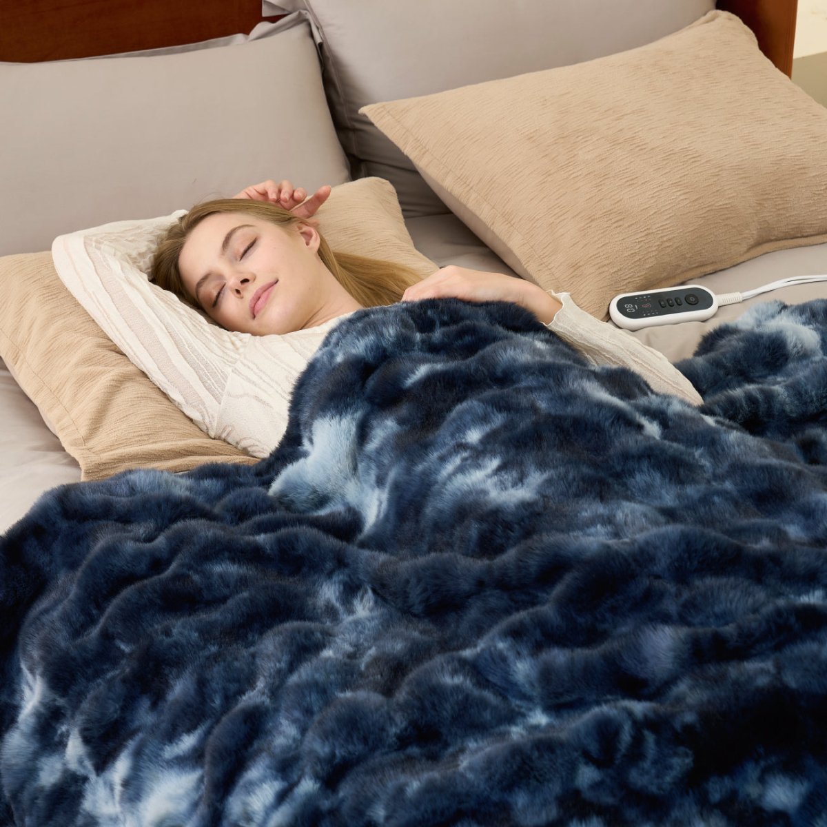 Woman sleeping under a tie-dye blue heated electric blanket with a remote control on a bed.  #color_Tie-dye Blue