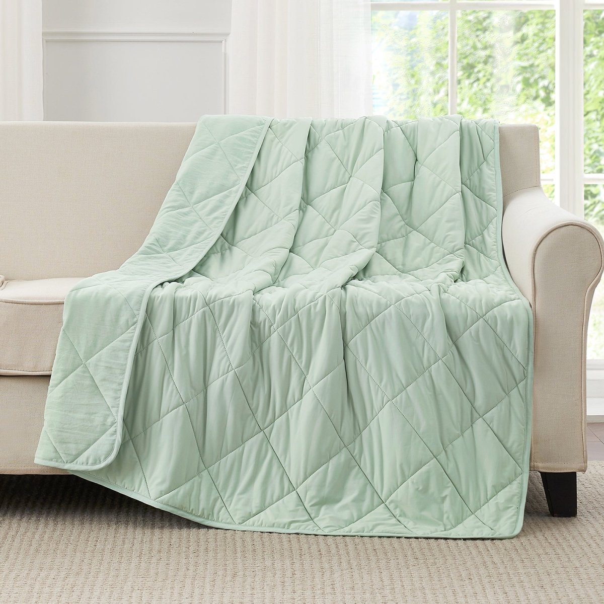 Light green quilt draped over a beige sofa in a bright room with large windows.  #color_Mint Green