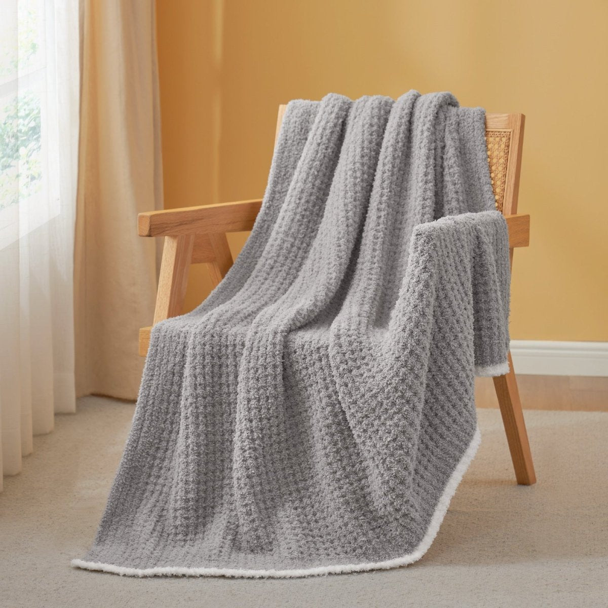 Soft Waffle Feather Yarn Throw Blanket in Grey draped over an armchair, creating a warm atmosphere. #color_Grey