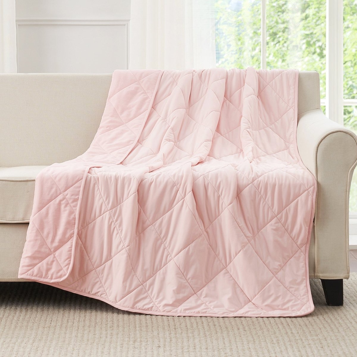Cool pink quilted blanket draped over a beige sofa in a bright room with large  windows. #color_Cool Pink