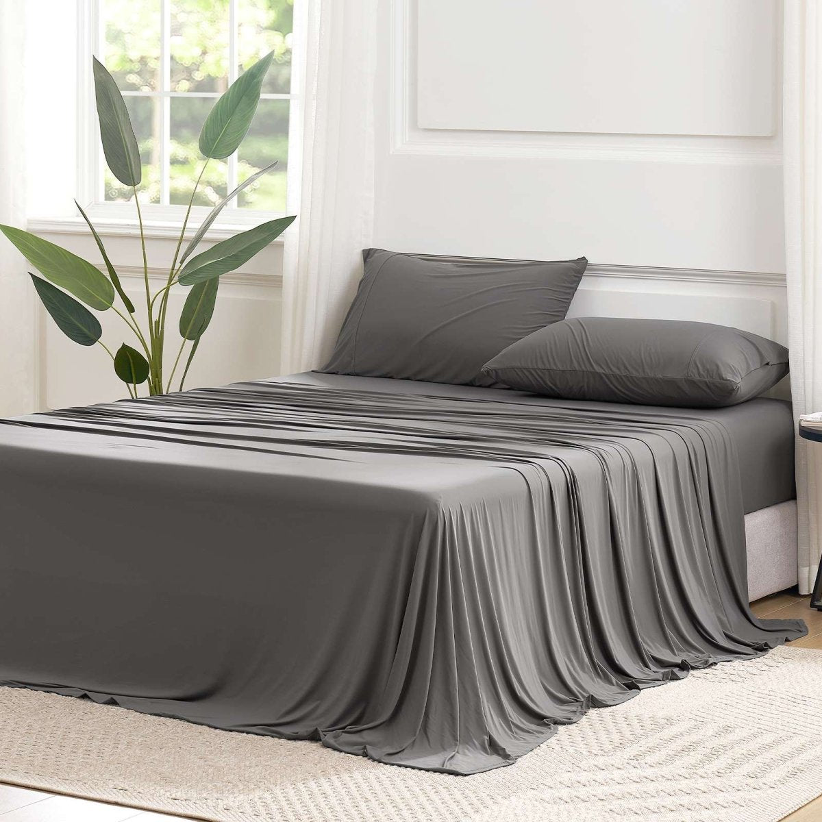 Cozy Bliss Outlast® Performance Cooling Sheet Set draped across a bed in a bright bedroom, showcasing the complete bedding appearance. #color_Dark Grey