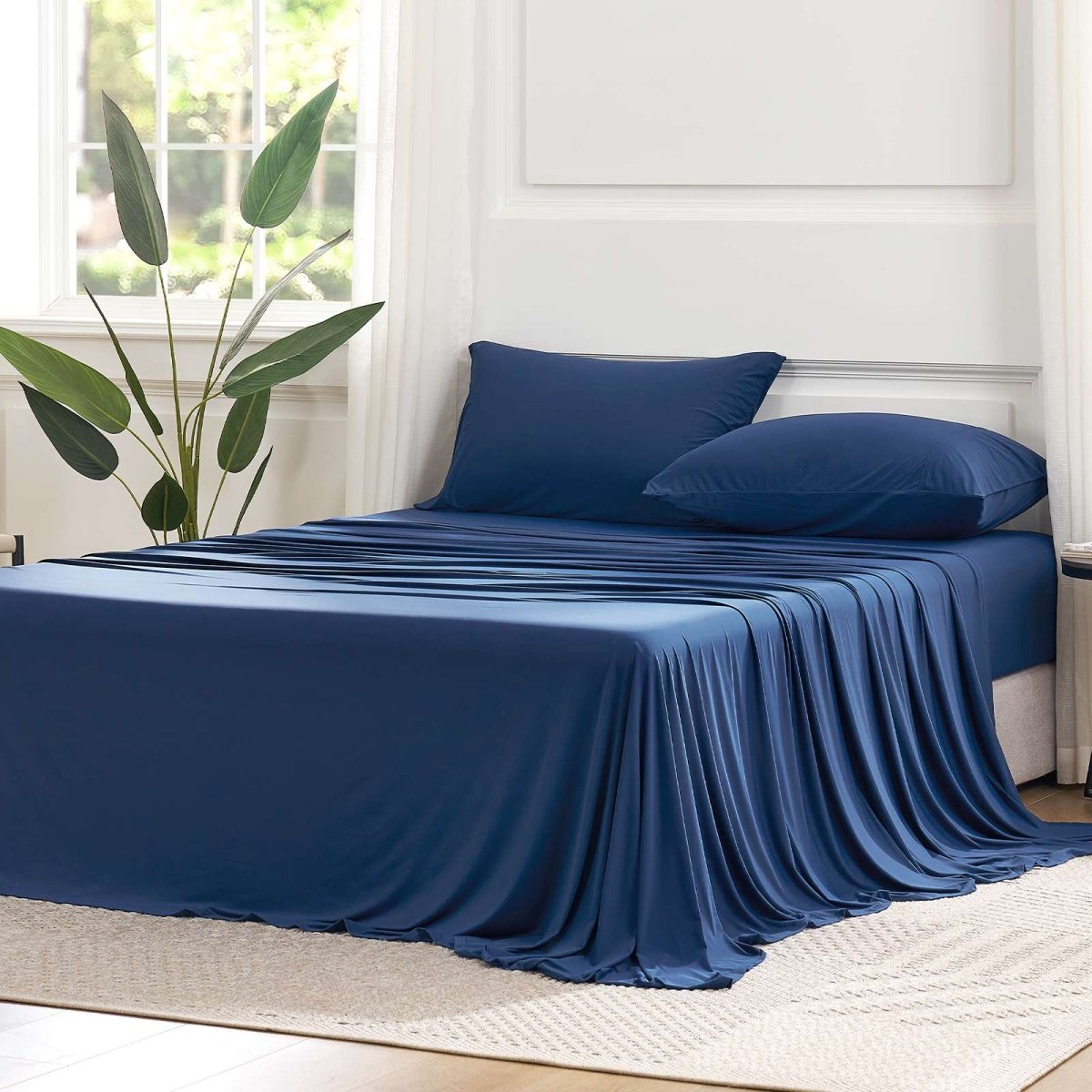 Cozy Bliss Outlast® Performance Cooling Sheet Set draped across a bed in a bright bedroom, showcasing the complete bedding appearance. #color_Navy Blue