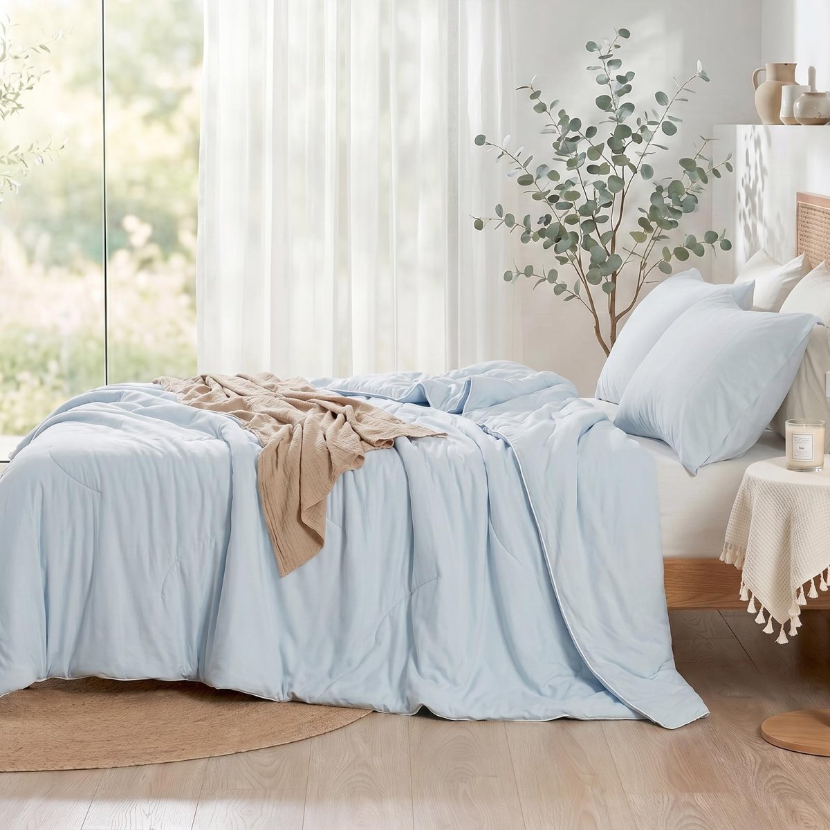 Cozy Bliss double-sided cooling comforter on a bed in a bright, sunlit bedroom with green plants, lightweight summer bedding for hot sleepers.#color_Cool Blue