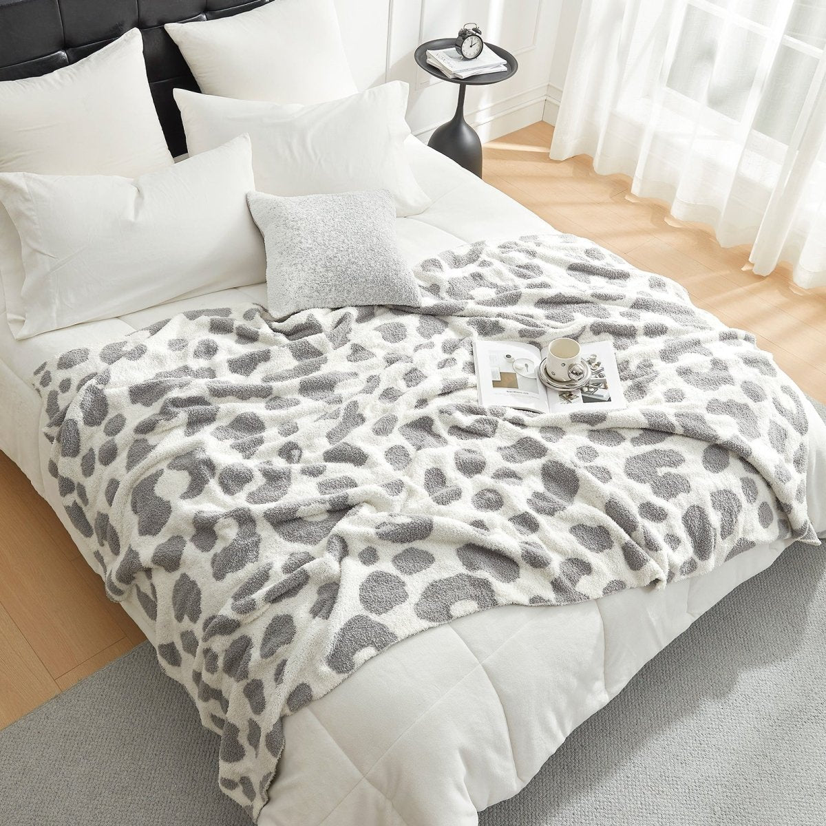 Reversible Leopard Feather Yarn Throw Blanket in Leopard Grey draped over a bed, creating a cozy atmosphere. #color_Leopard Grey