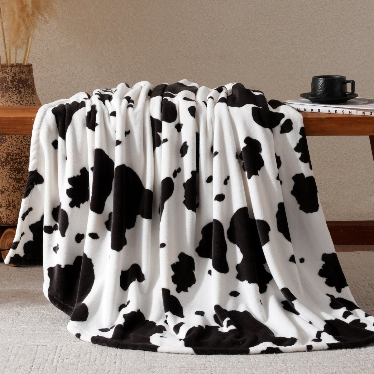 Cow print milkyplush throw blanket in Black & White draped over a desk #color_Black & White