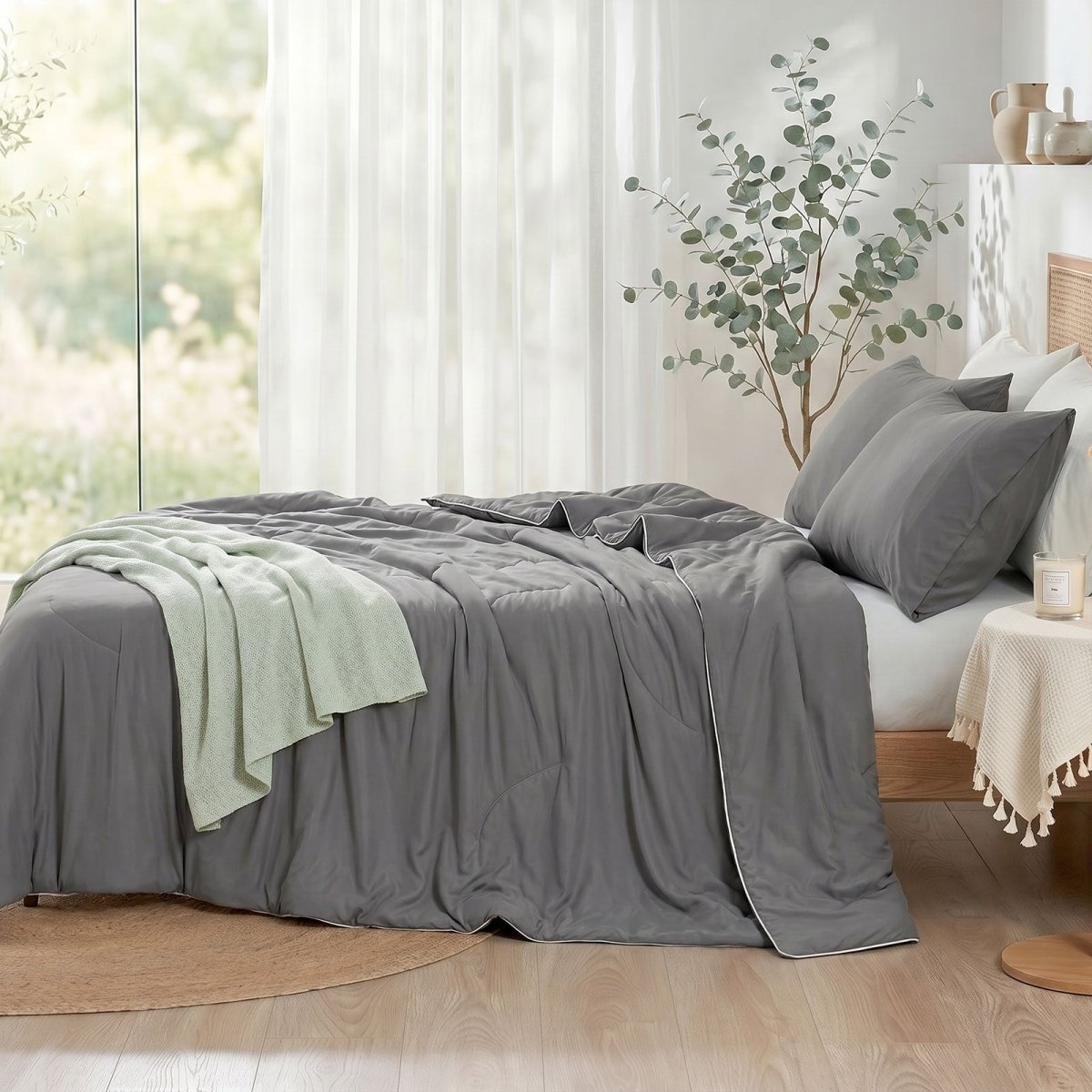 Cozy Bliss double-sided cooling comforter on a bed in a bright, sunlit bedroom with green plants, lightweight summer bedding for hot sleepers.#color_Dark Grey