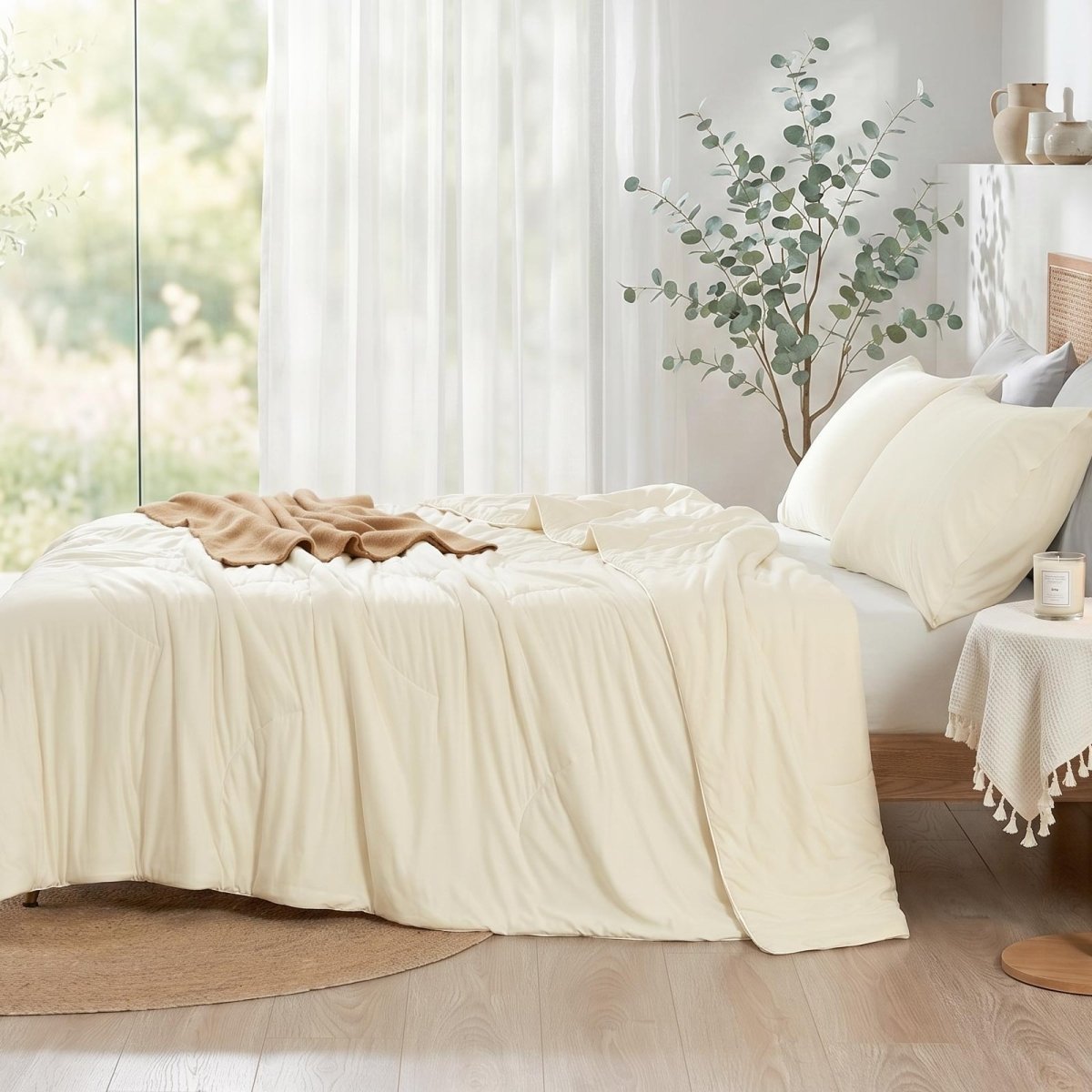 Cozy Bliss double-sided cooling comforter on a bed in a bright, sunlit bedroom with green plants, lightweight summer bedding for hot sleepers.#color_Ivory