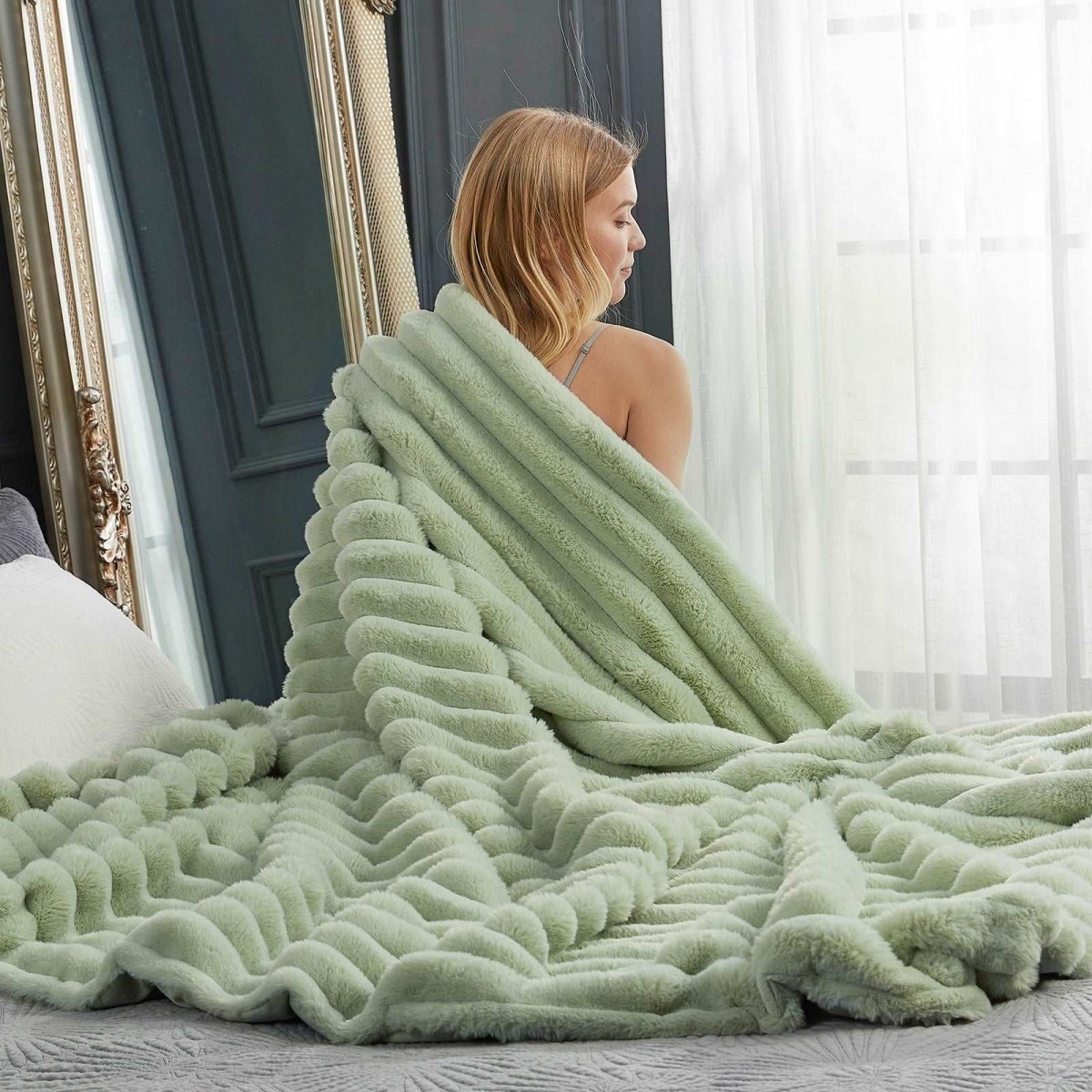 Woman sitting on bed with Sage green striped faux fur blanket, ultra-soft cozy blanket for comfortable relaxation, cozy bedding. #color_Sage Green