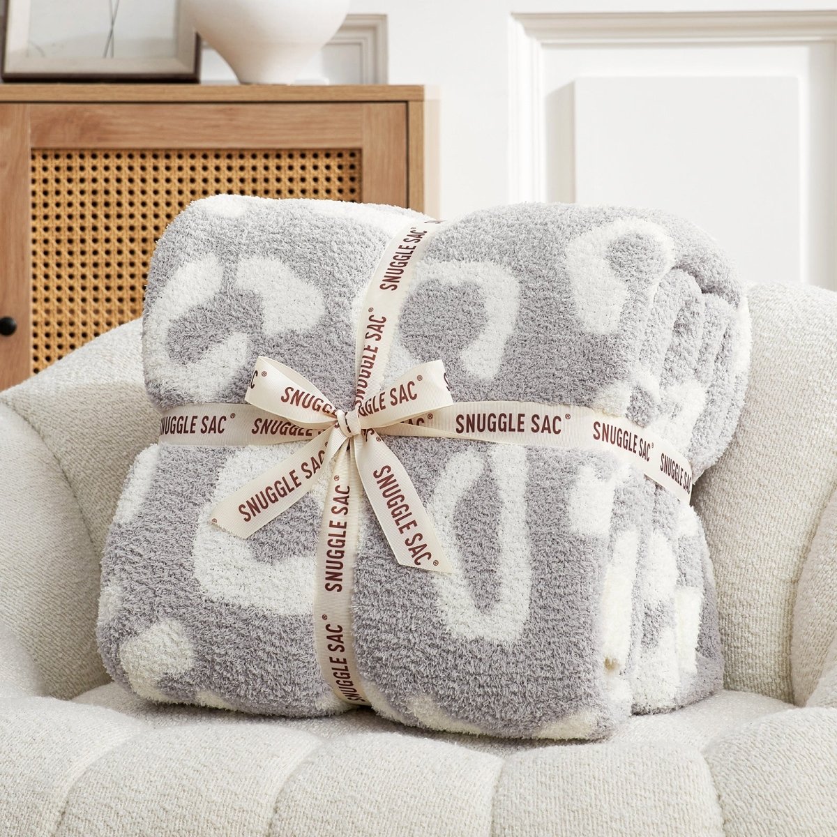 Woman lounging on a sofa with a Reversible Leopard Feather Yarn Throw Blanket in Leopard Grey, offering warmth and comfort. #color_Leopard Grey