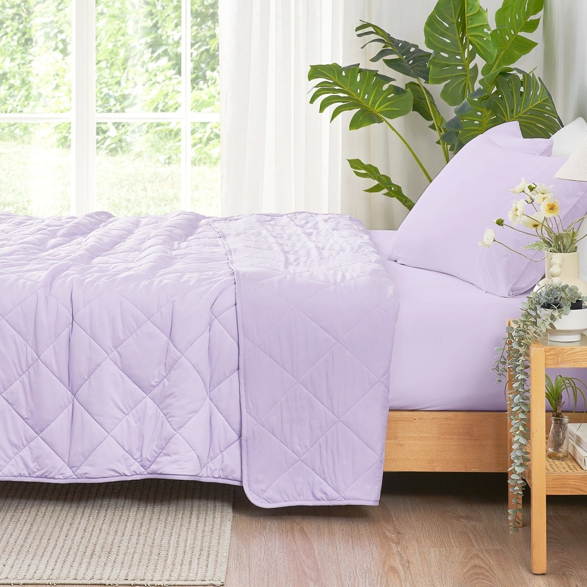 Bed with a purple quilt and pillows in a bright room with plants  #color_Purple