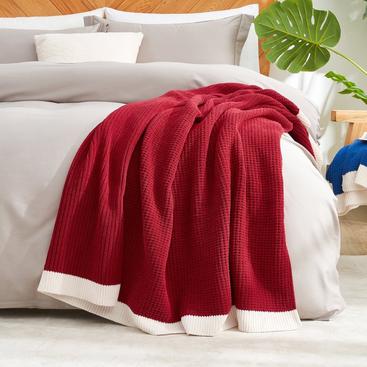 Red blanket on a bed with white bedding and a plant in the corner. #color_Christmas Red