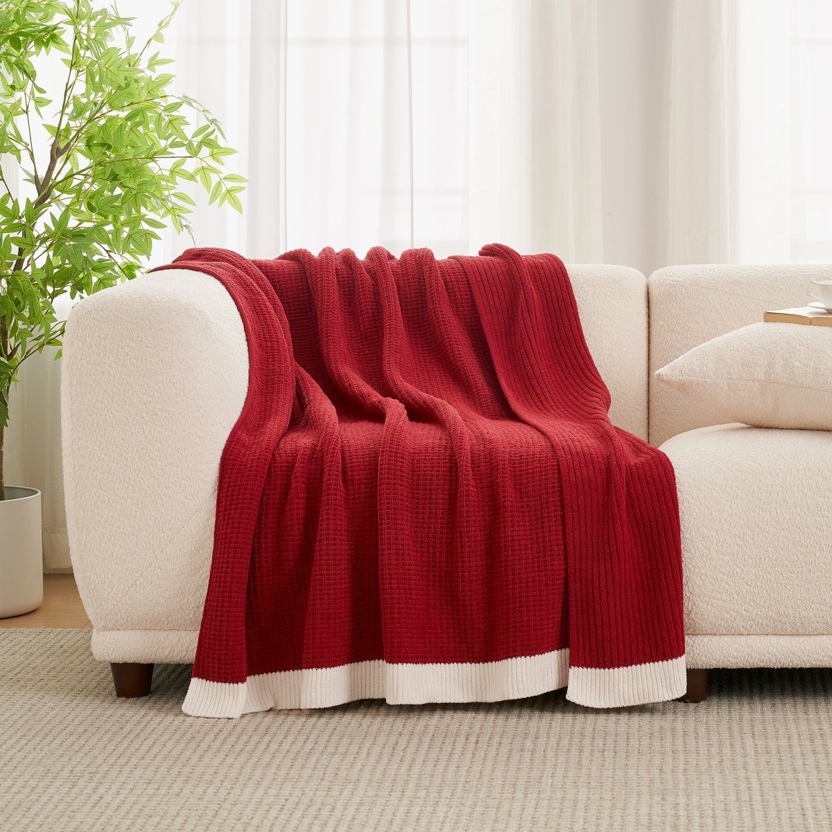 Red blanket draped over a beige sofa in a living room setting with a plant and curtains. #color_Christmas Red
