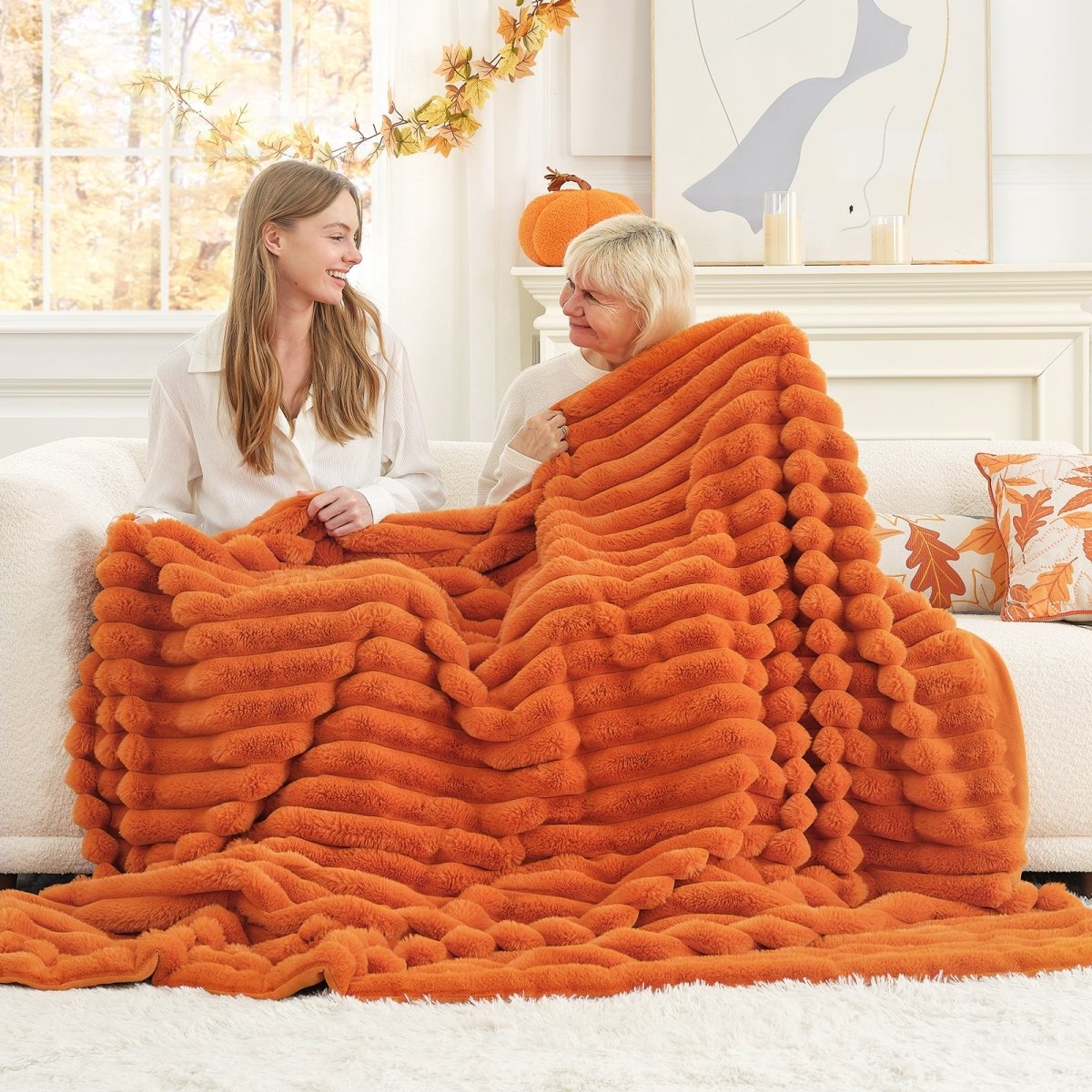 Mom and daughter women sitting on a couch under an orange fluffy blanket in a cozy living room.  #color_Burnt Orange