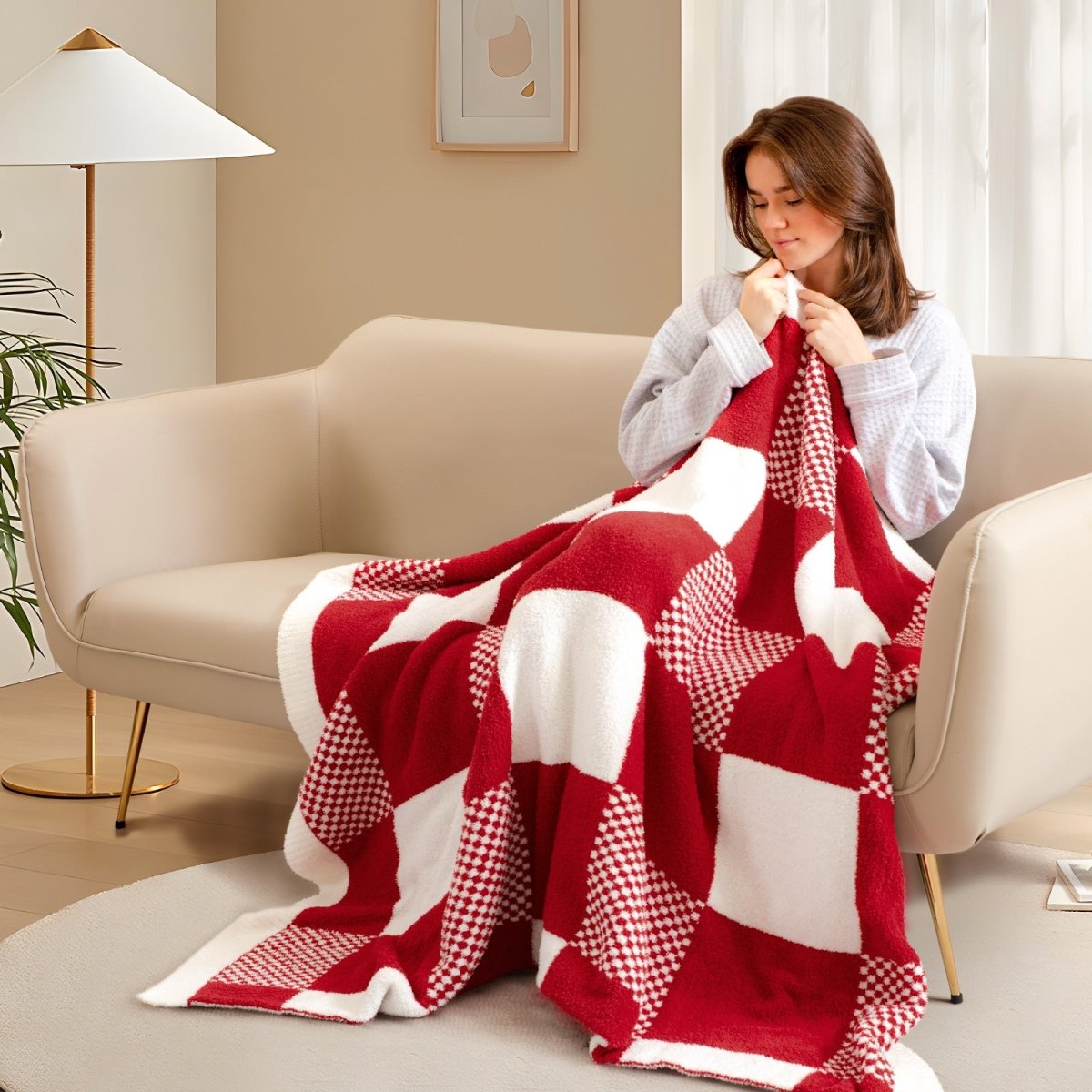 Woman relaxing on a sofa while using Checkered Feather Yarn Throw Blanket in Red & Cream in a cozy room setting. #color_Red & Cream