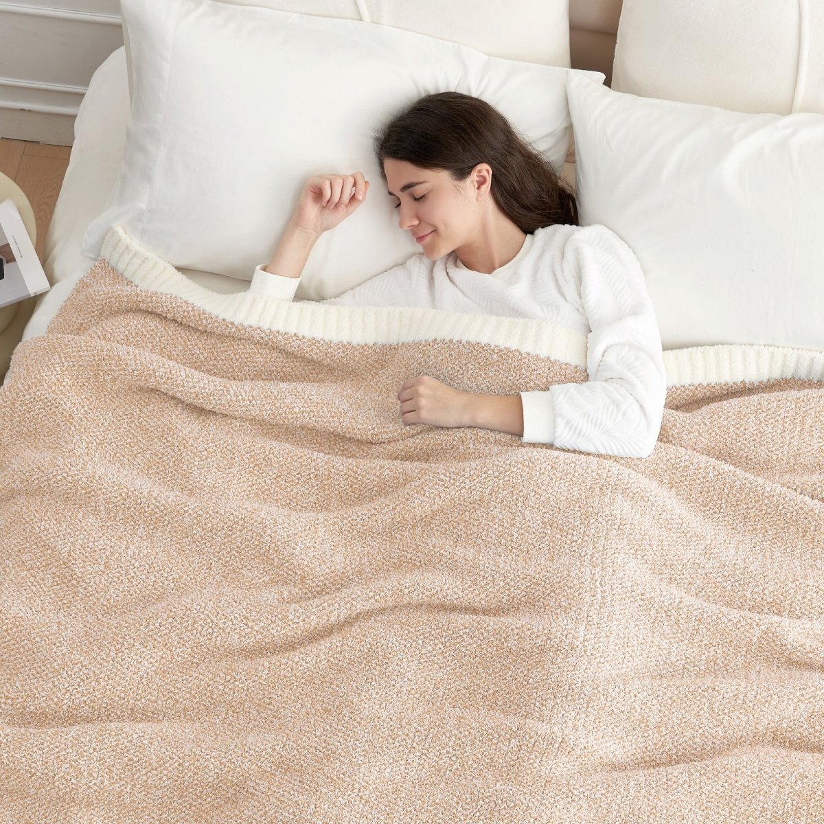 Woman lying on a bed with a Heather Feather Yarn Throw Blanket in Beige, ideal for rest. #color_Beige