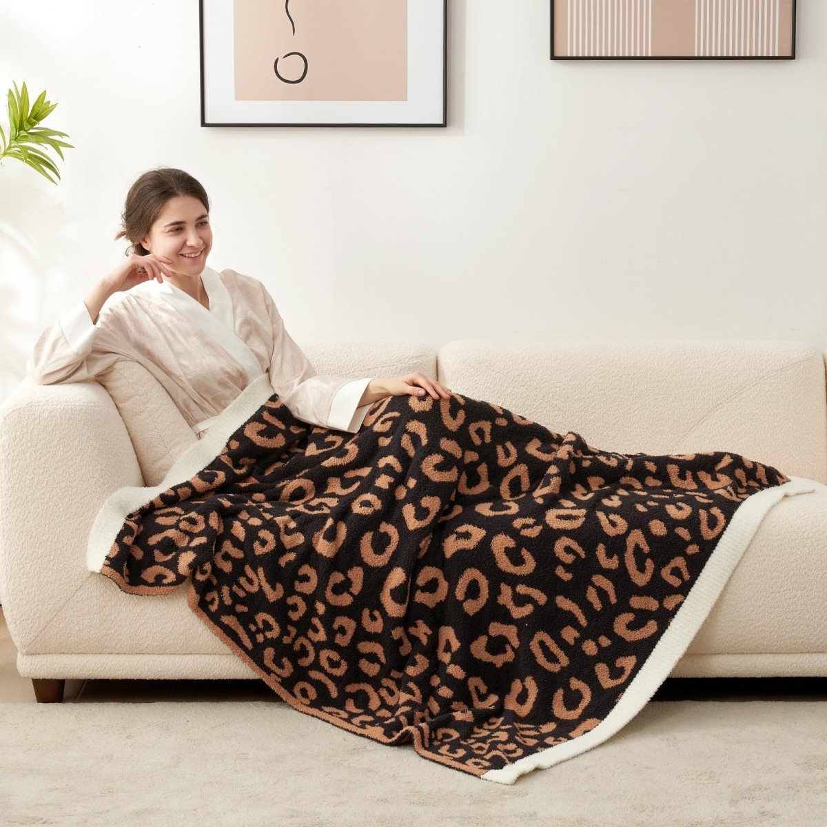 Woman relaxing on a sofa under a Reversible Leopard Feather Yarn Throw Blanket in Brown Leopard, enjoying cozy comfort. #color_Brown Leopard