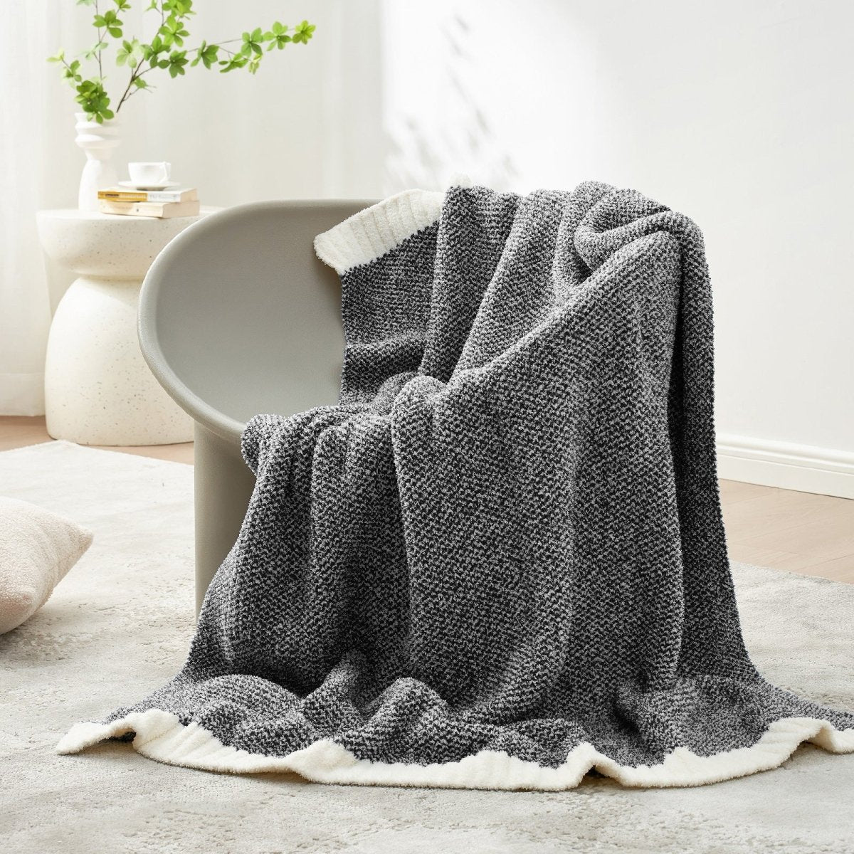 Heather Feather Yarn Throw Blanket in Black draped over a chair, adding a sleek and cozy touch. #color_Black