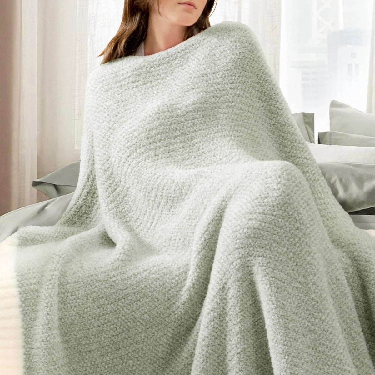 Woman wrapped in a Heather Feather Yarn Throw Blanket in Sage Green, relaxing comfortably. #color_Sage Green